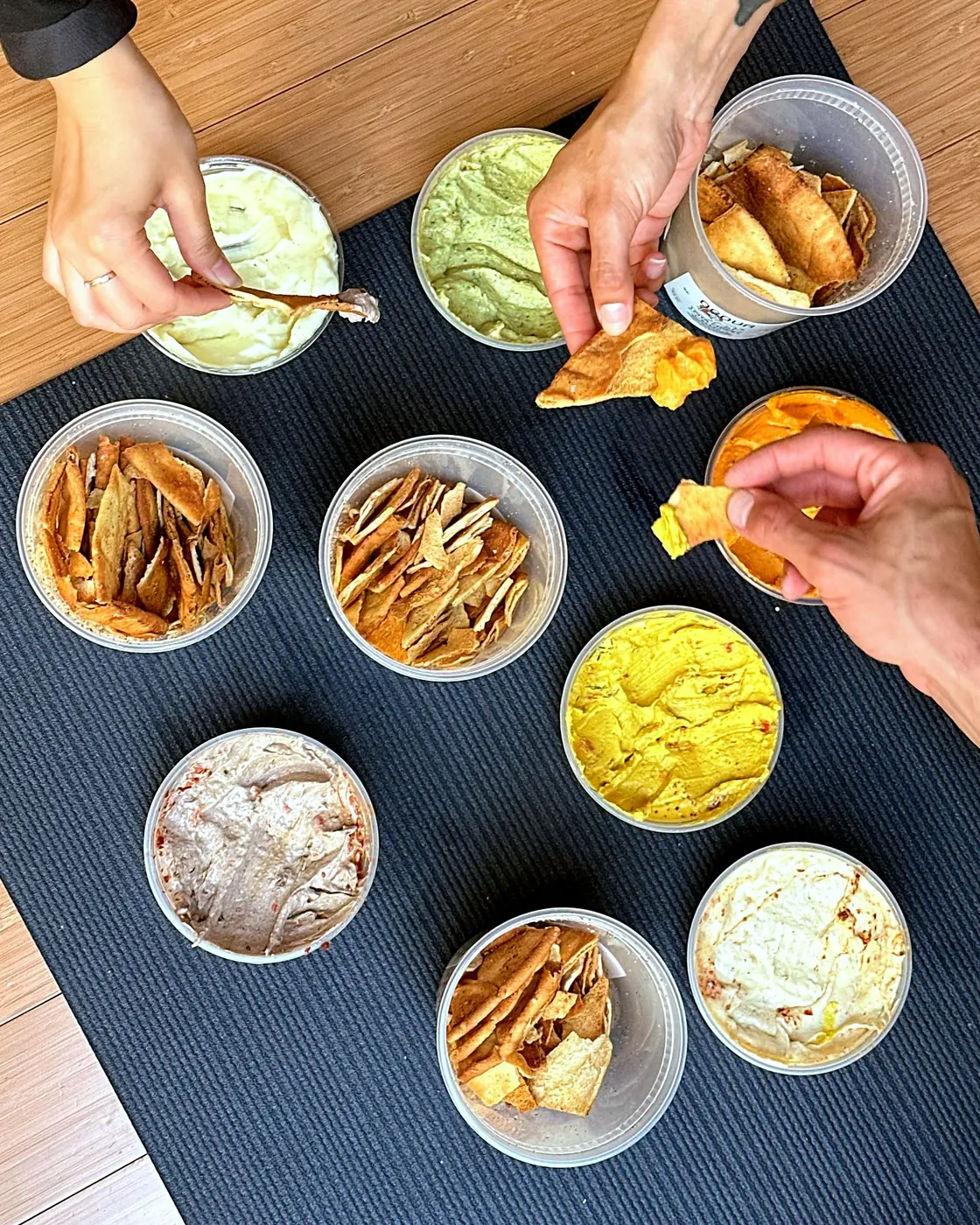 Friends dipping pita chips into tubs of Obour hummus and toum